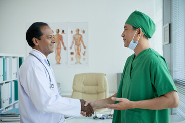 Surgeon in green scrubs shaking hand of chief physician when meeting with his in office