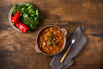 Traditional goulash meat in ceramic bowl with pepper and herbs, fork and napkin. Top view, copy space