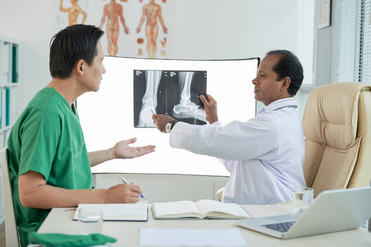 Serious physician discussing tumor on feet of patient when looking at x-ray image