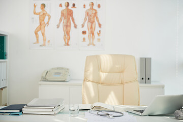 Desk of chief physician with laptop, planner, printed cardiograms and folders with medical histories of patients