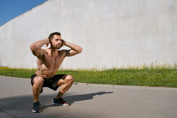 Athletic man doing squat exercise outdoors