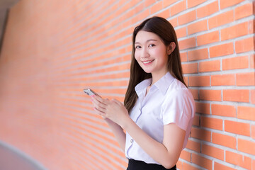Portrait of an Asian Thai female student in a uniform is smiling happily while using a smartphone...
