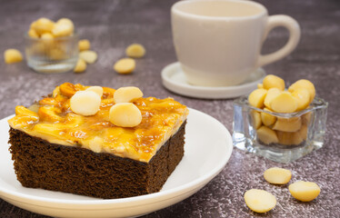 Toffee chocolate cake slice on plate with macadamia seeds in small bowl and coffee cup on stone background for dessert break