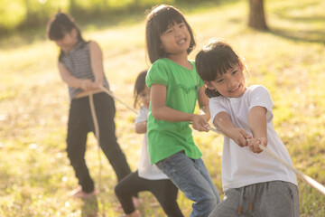 Fototapeta premium Children playing tug of war at the park on sunsut