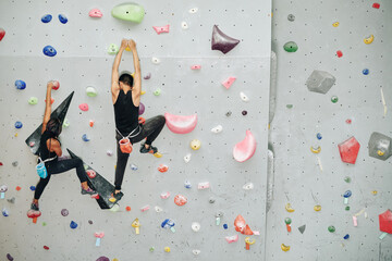 Young couple climbing up the wall when training for competition at indoor bouldering facility