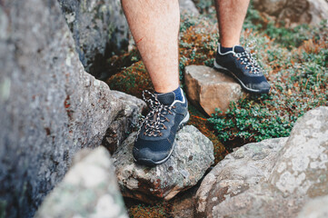The hiker walks over the rocks in the mountains. Man's legs in shoes close-up.