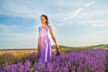 girl in a purple dress with a wreath and ribbons on her head in a lavender field at sunset. Boho style