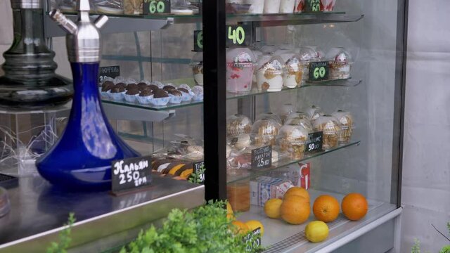 Sweet Desserts, Pastries, Fruits are Sold on Glass Showcase of the Bakery. Delicate mousses, cakes, cookies, hookah are stored for sale on shelves. Goods are labeled with price tags. Trade Food. 4K.
