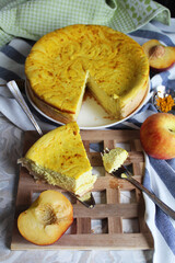Bright yellow lemon cottage cheese and peach pie on a plate. Piece of cake. A piece of pie on a metall spatula and little fork. Striped blue and white towel, wood stand, peach. 