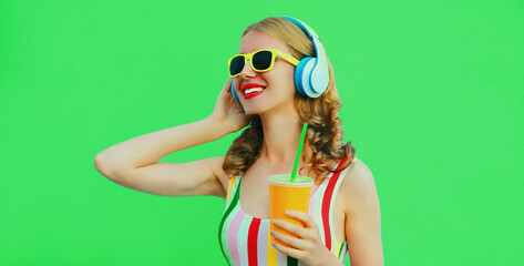 Portrait of happy smiling young woman listening to music in headphones with fresh cup of juice on...