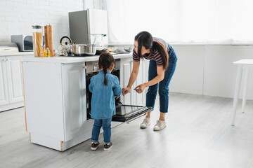 Asian mother and child standing near open oven in kitchen