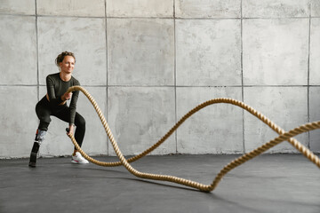 Young sportswoman with prosthesis working out with battle ropes