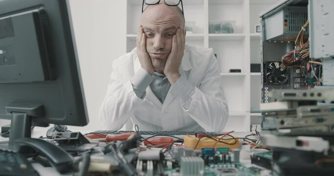 Stressed frustrated computer repair technician sitting at desk