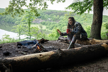 Girl with a cup of hot drink near the fire in nature.