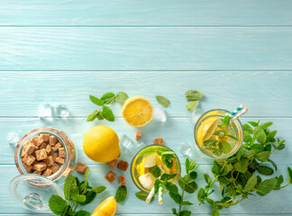 Summer cold drinks in glasses with lemons, mints on blue wooden background. Top view of lemonade with cane sugar and paper straws for drinks. Copy space.