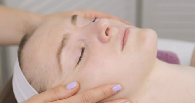 Lymphatic drainage modeling facial massage. Young woman in spa salon at facebuilding session. Beautiful hands of the masseur. Close up