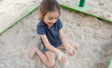 Funny little girl playing with sand in the sandbox.