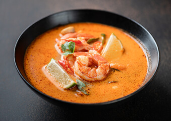Tom Yum kung Spicy Thai soup with shrimp in a black bowl on a dark background, selective focus