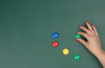 female hand attaches multi-colored magnets to a green board