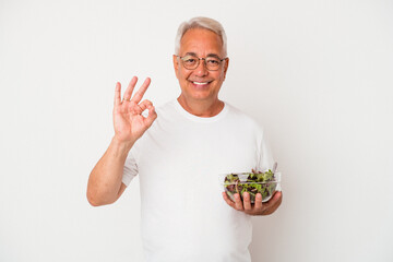 Senior american man eating salad isolated on white background cheerful and confident showing ok...