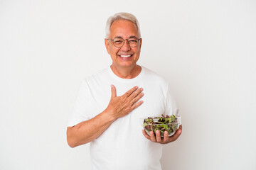 Senior american man eating salad isolated on white background laughs out loudly keeping hand on...