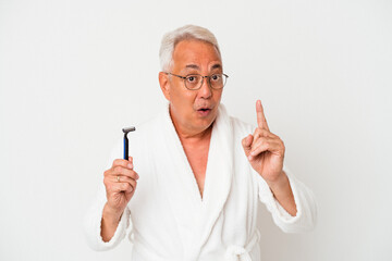 Senior american man wearing bathrobe holding razor blade isolated on white background having an idea, inspiration concept.