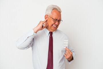 Senior american man holding pills isolated on white background covering ears with hands.