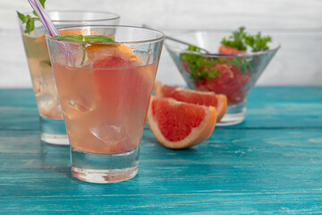 Cocktail with grapefruit on a light background with a sprig of mint and ice cubes.