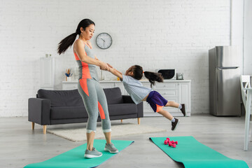 Asian woman spinning daughter near fitness mats at home