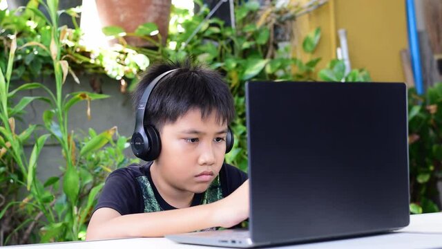 Asian Boy Wearing Headphones And Black Shirt Playing A Games On His Smart Phone.