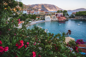 Assos village in evening light on Kefalonia, Greece. Red flower blossom in front of turquoise bay and colorful traditional houses