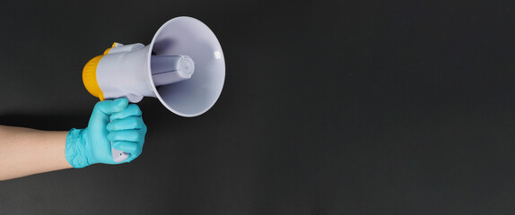 Megaphone in hand and wearing blue latex glove on black background. Studio shooting.