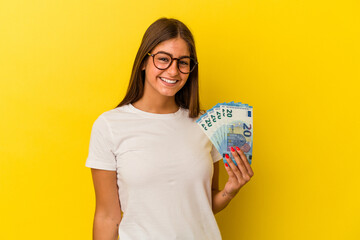 Young caucasian woman holding bills isolated on yellow background happy, smiling and cheerful.