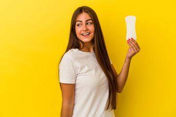 Young caucasian woman holding a compress isolated on yellow background looks aside smiling,...