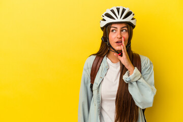 Young student caucasian woman wearing a bike helmet isolated on yellow background is saying a secret hot braking news and looking aside