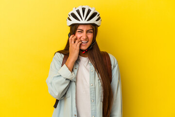Young student caucasian woman wearing a bike helmet isolated on yellow background biting fingernails, nervous and very anxious.