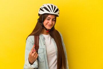 Young student caucasian woman wearing a bike helmet isolated on yellow background pointing with finger at you as if inviting come closer.