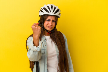 Young student caucasian woman wearing a bike helmet isolated on yellow background showing fist to camera, aggressive facial expression.