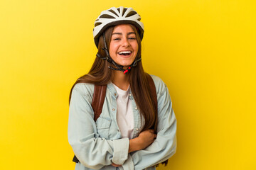 Young student caucasian woman wearing a bike helmet isolated on yellow background laughing and having fun.