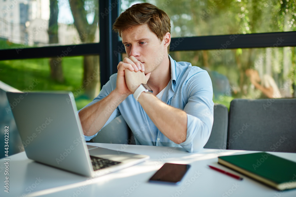 Poster pensive male student 20s watching education webinar on modern laptop computer using 4g wireless in c