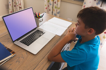 Caucasian boy having video call during class on laptop with copy space, sitting at desk at home