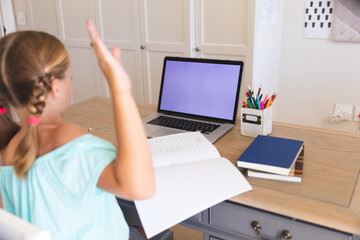 Caucasian girl having video call during class on laptop with copy space and raising hand at home