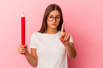 Young caucasian woman holding a big pencil isolated on pink background showing number one with...