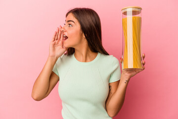 Young caucasian woman holding a pasta jar isolated on pink background shouting and holding palm near opened mouth.