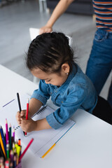 Asian girl drawing near blurred color pencils and parent at home