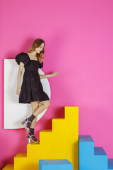 Young pleasing woman in a black dress poses in the studio against a pink wall