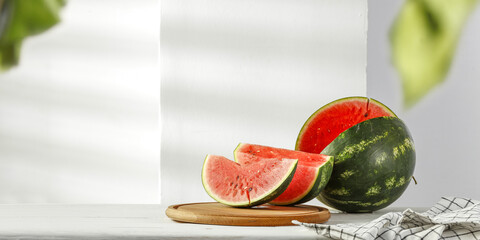 Fresh watermelon on white desk and wall with shadows 