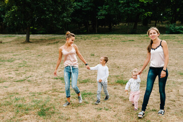 Obraz premium Two mothers with kids walking on nature on summer day. Mom and son, daughter walk in the park. Concept of happy family. Close Up.
