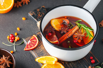 Mulled wine or punch in cooking pot and mugs with ingredients on dark background.
