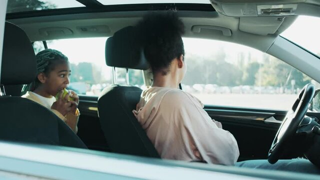 A happy african american woman is talking to her child sitting in the car seat before driving the car